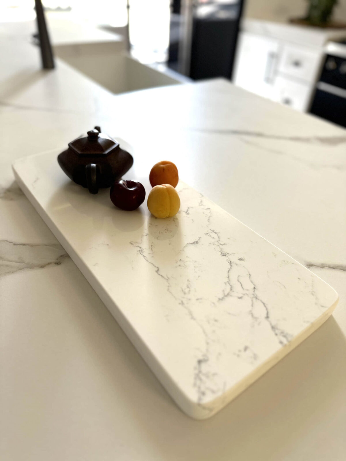 Marble countertop with teapot and three small fruits.