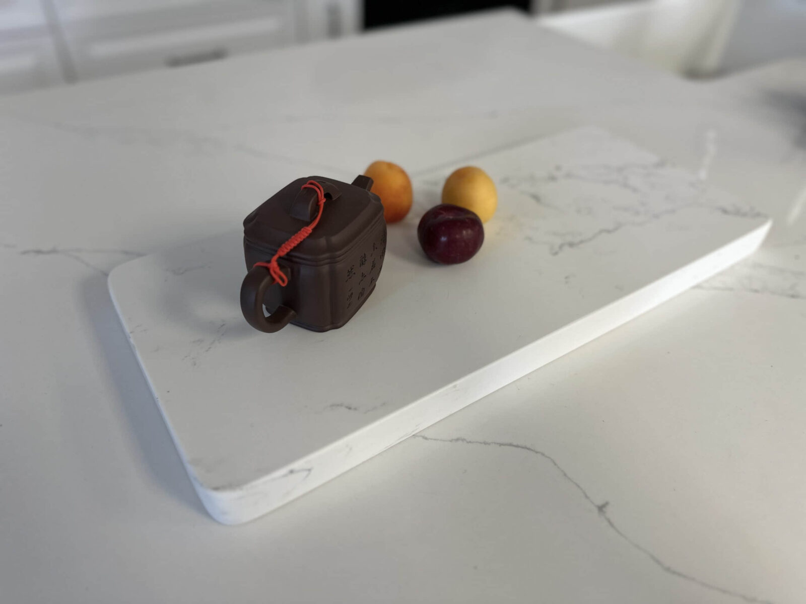Teapot and fruit on a white marble cutting board.