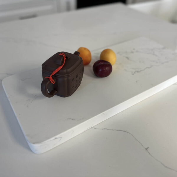 Teapot and fruit on a white marble cutting board.