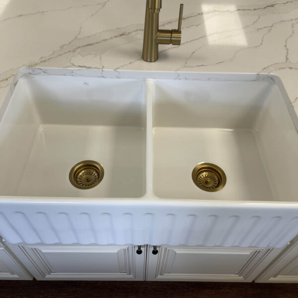 White double kitchen sink with brass fixtures on marble countertop.