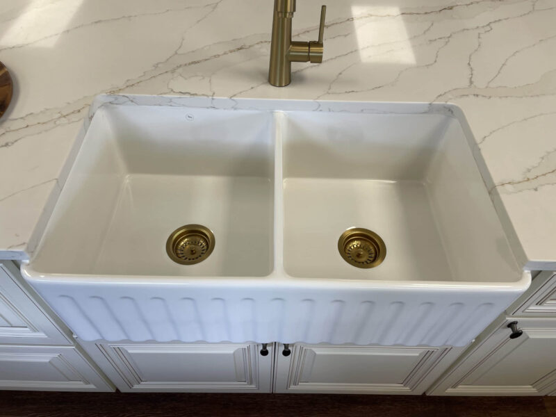 White double kitchen sink with brass fixtures on marble countertop.