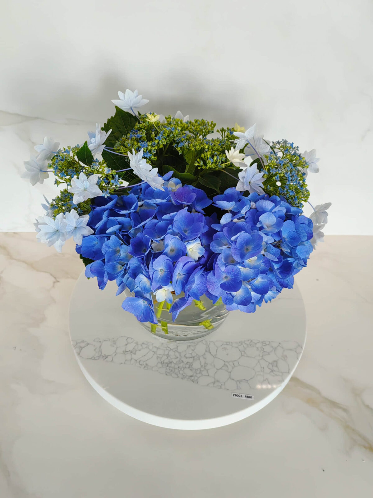 Blue and white hydrangea bouquet in a glass vase on marble surface.