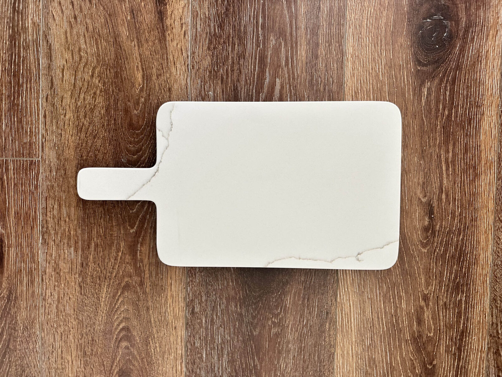 White marble cutting board on wooden surface.