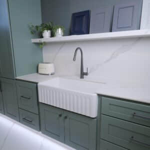 Modern kitchen with green cabinets, white countertop, and farmhouse sink.