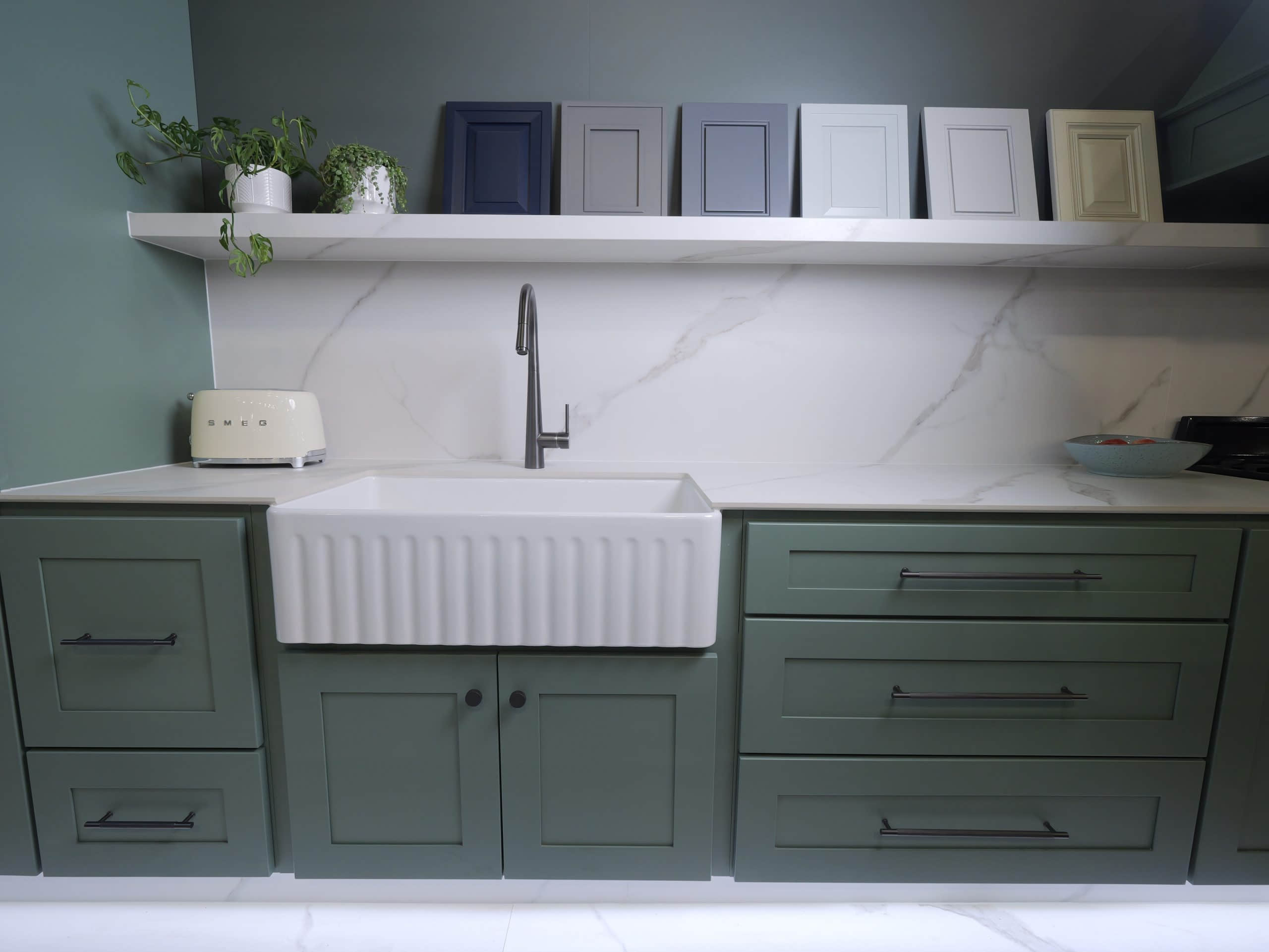 Modern kitchen with green cabinets, white sink, and decorative frames on shelf.
