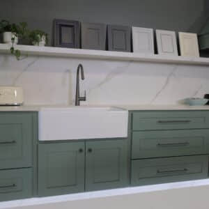 Green kitchen cabinets with a white sink and decorative frames above.