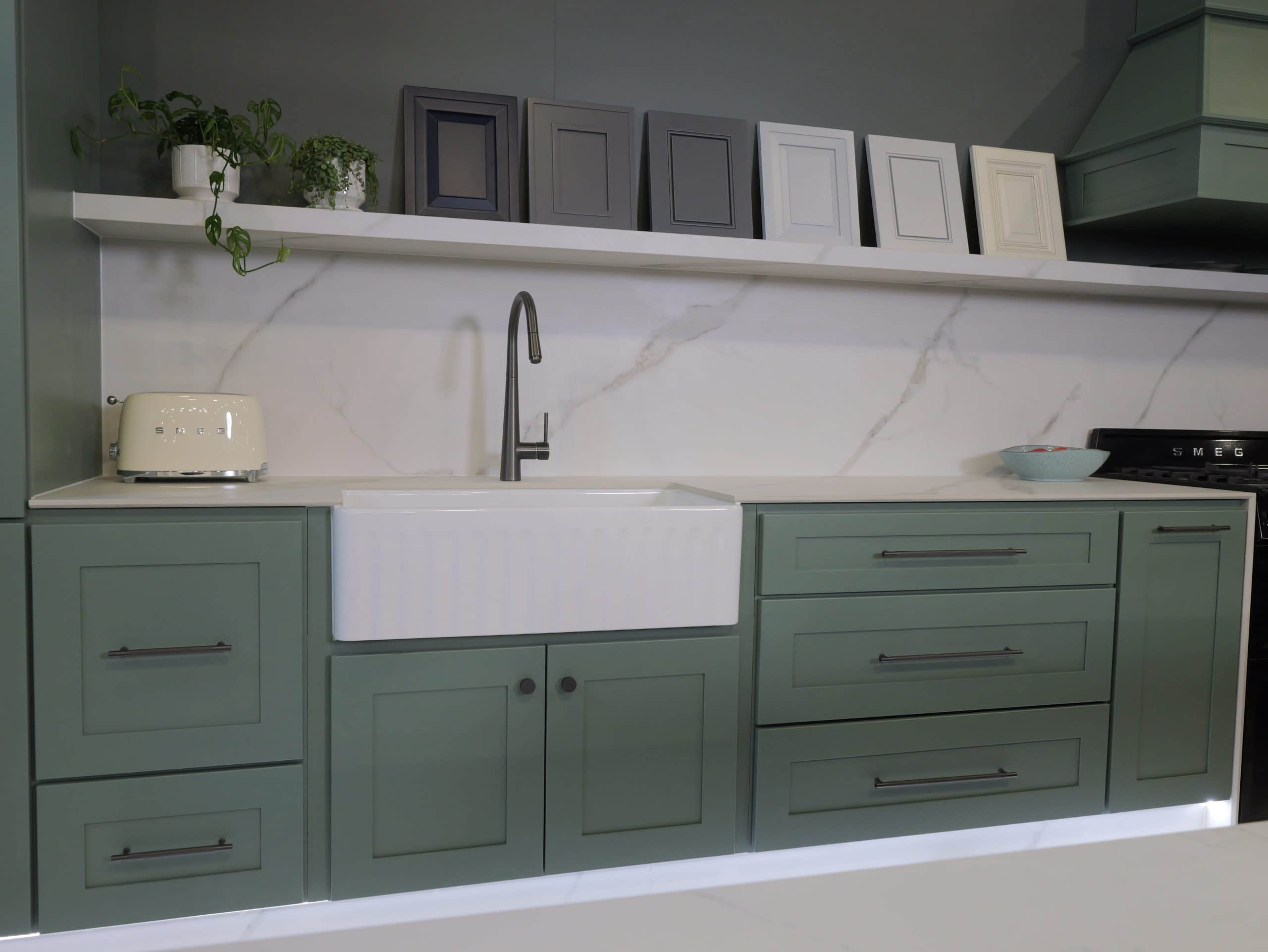 Green kitchen cabinets with a white sink and decorative frames above.