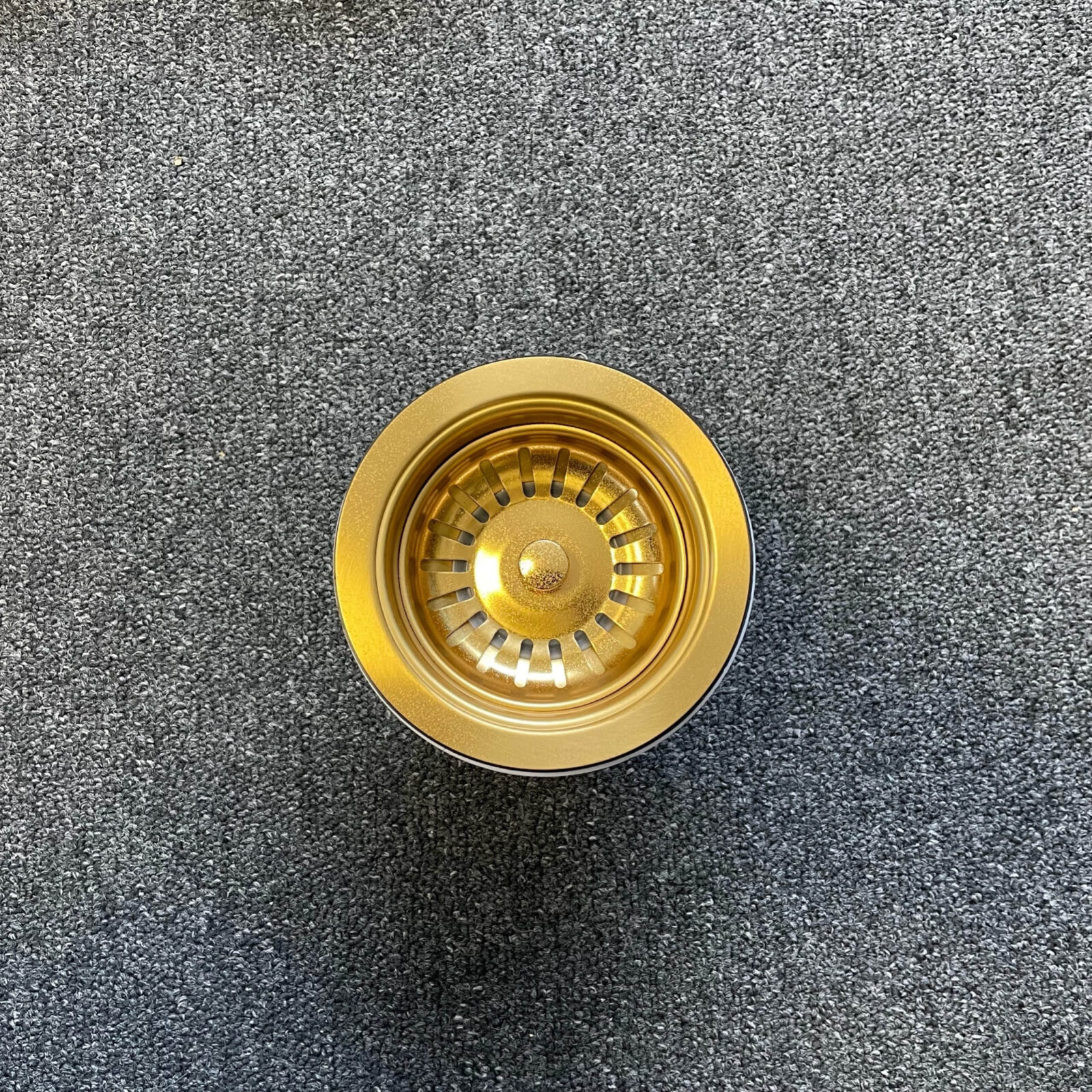 Gold stainless steel strainer on gray carpet, top view.