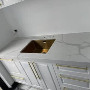 White kitchen countertop with gold sink and handles.