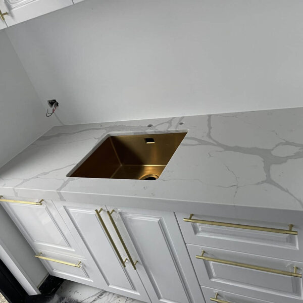 White kitchen countertop with gold sink and handles.