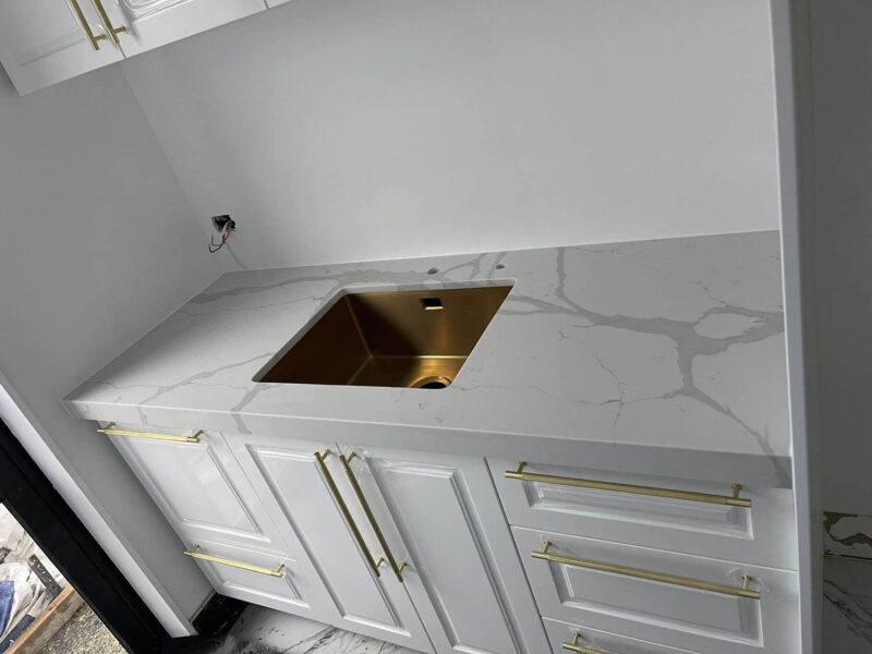 White kitchen countertop with gold sink and handles.