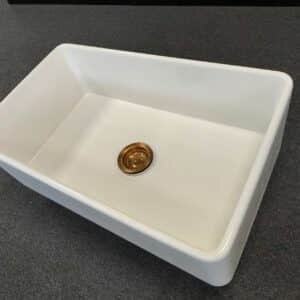 White rectangular kitchen sink with a gold drain on dark countertop.
