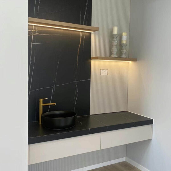 Modern bathroom vanity with black sink and gold faucet.