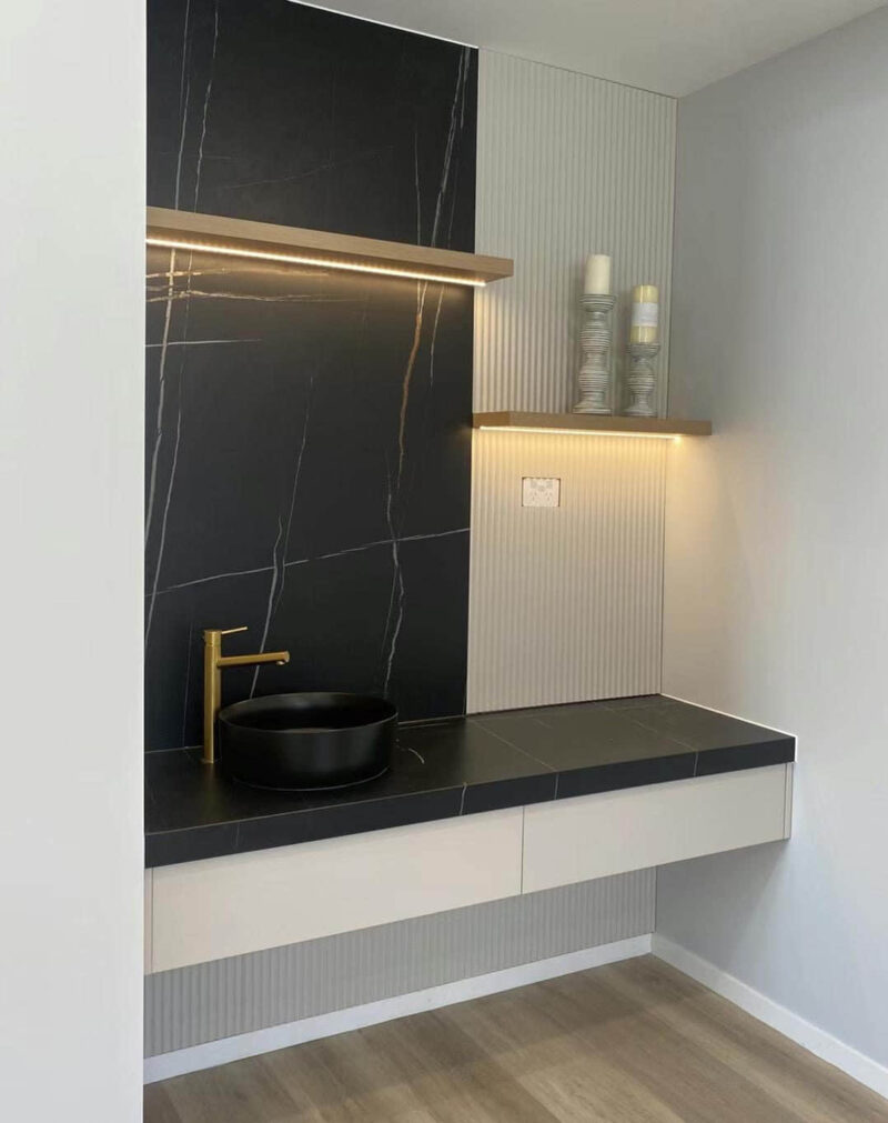 Modern bathroom vanity with black sink and gold faucet.